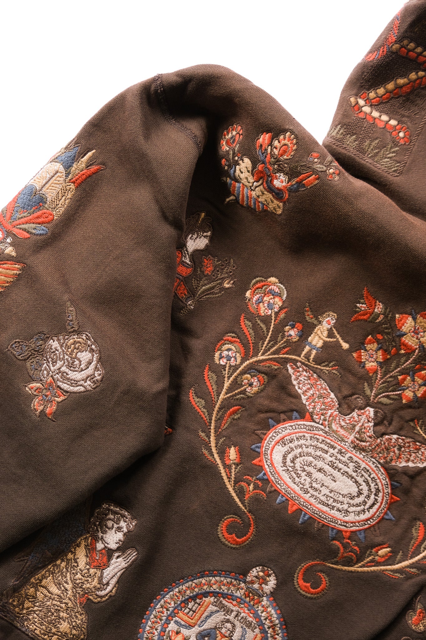 Close-up of a dark brown embroidered textile with ornate floral motifs, birds, and decorative oval medallions in red, beige, blue, and white thread.