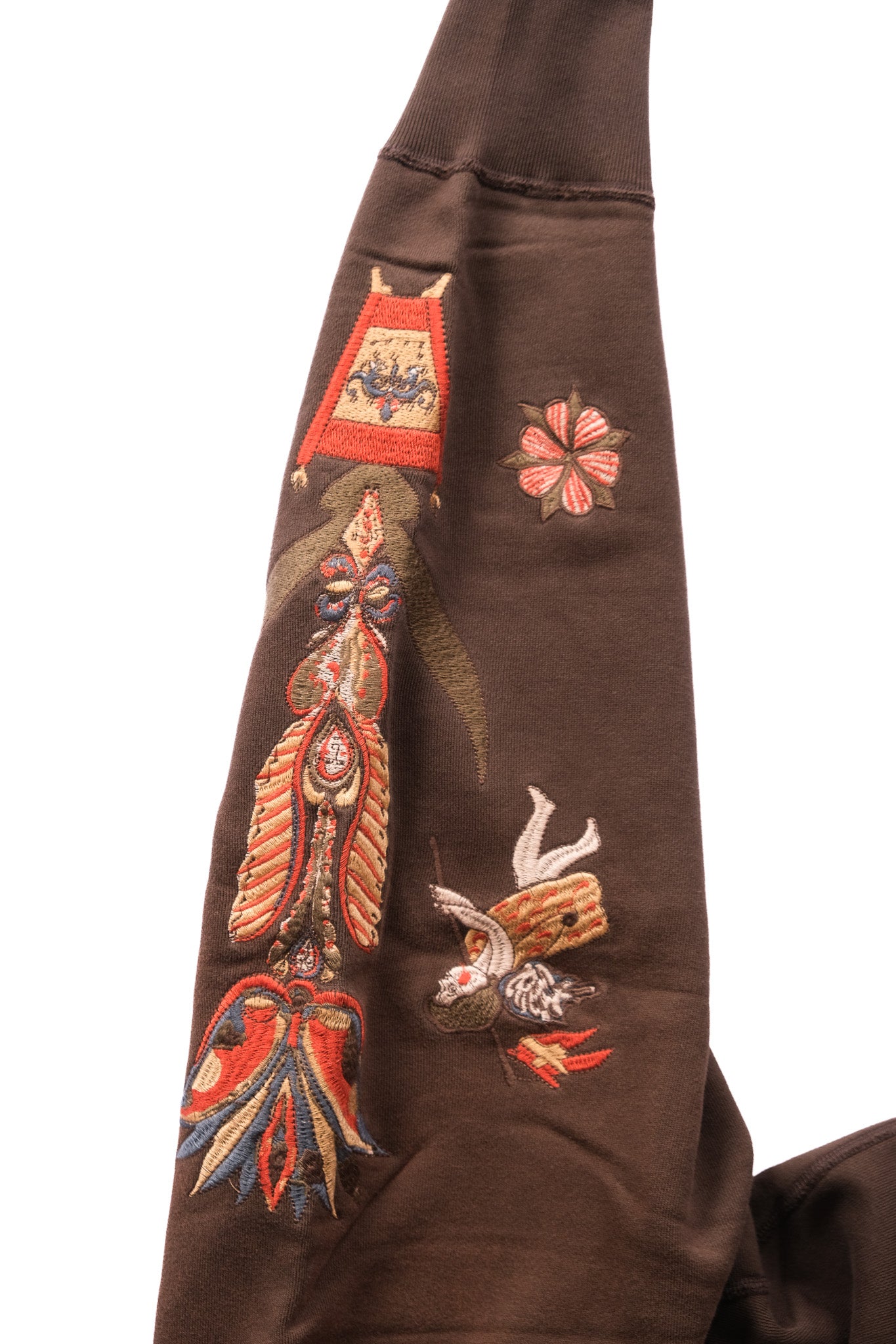 A close-up of a brown garment sleeve featuring detailed multicolor embroidery with a large figure, and floral motifs on a plain white background.
