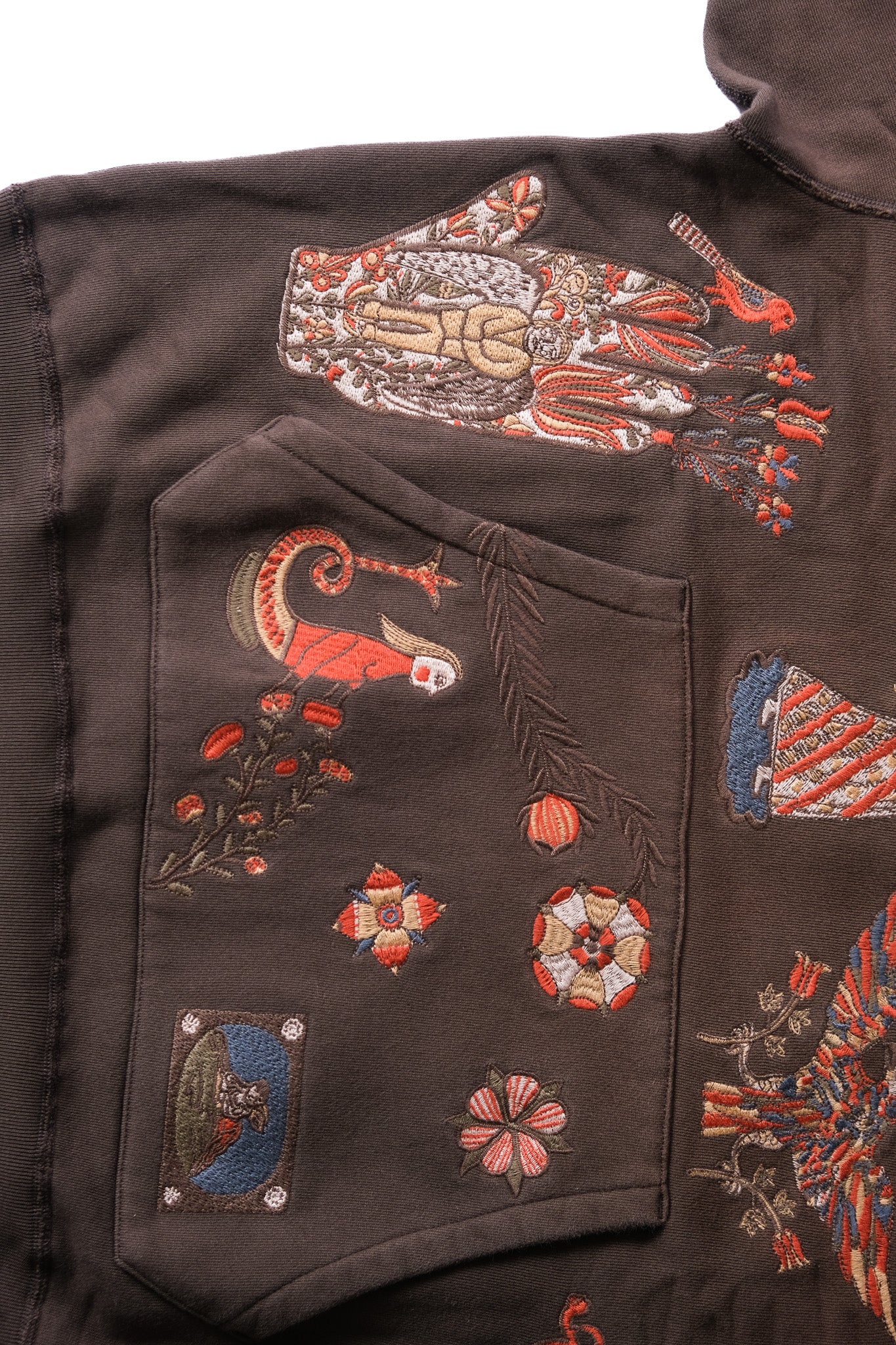 Close-up of a dark brown embroidered hoodie, featuring a large multicolor hand patch and various floral and bird motifs on the front pocket and body.