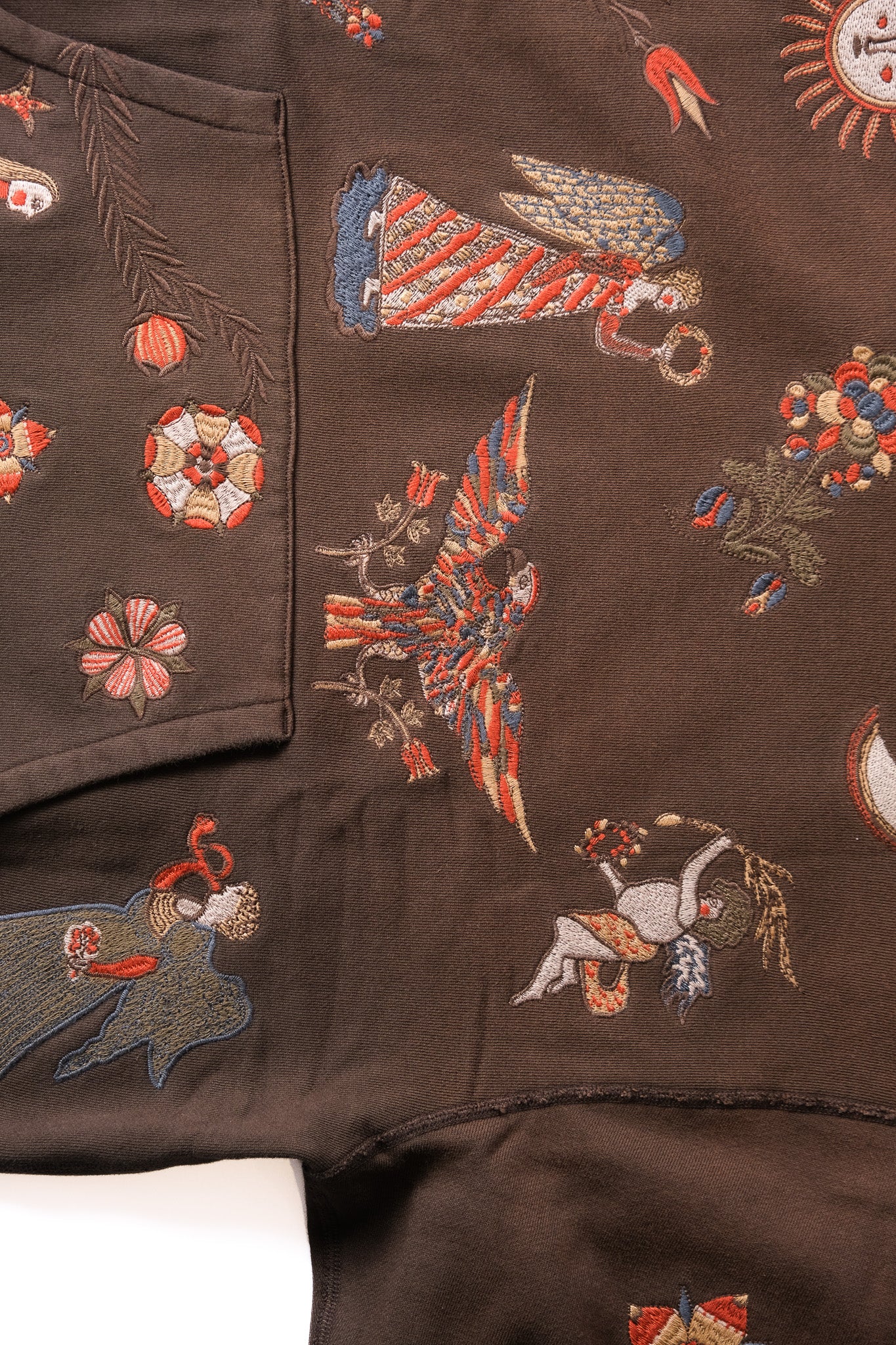 Close-up of a dark brown embroidered garment featuring colorful stitched motifs including angels, flowers, and celestial designs.