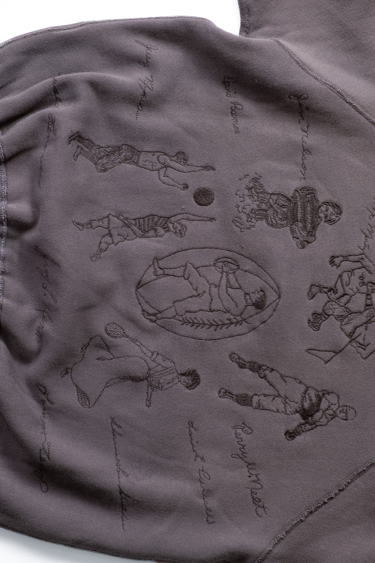 A close-up of a dark gray sweatshirt featuring a detailed black line-art graphic of football players and handwritten script across the chest.